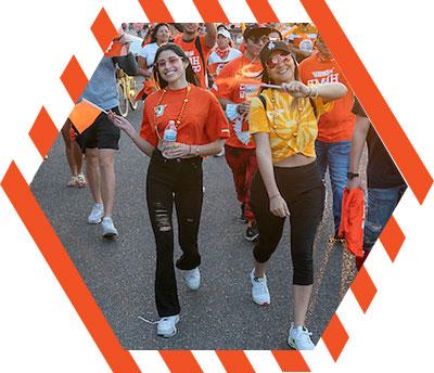 Two female student walking in the Homecoming parade waving orange flags